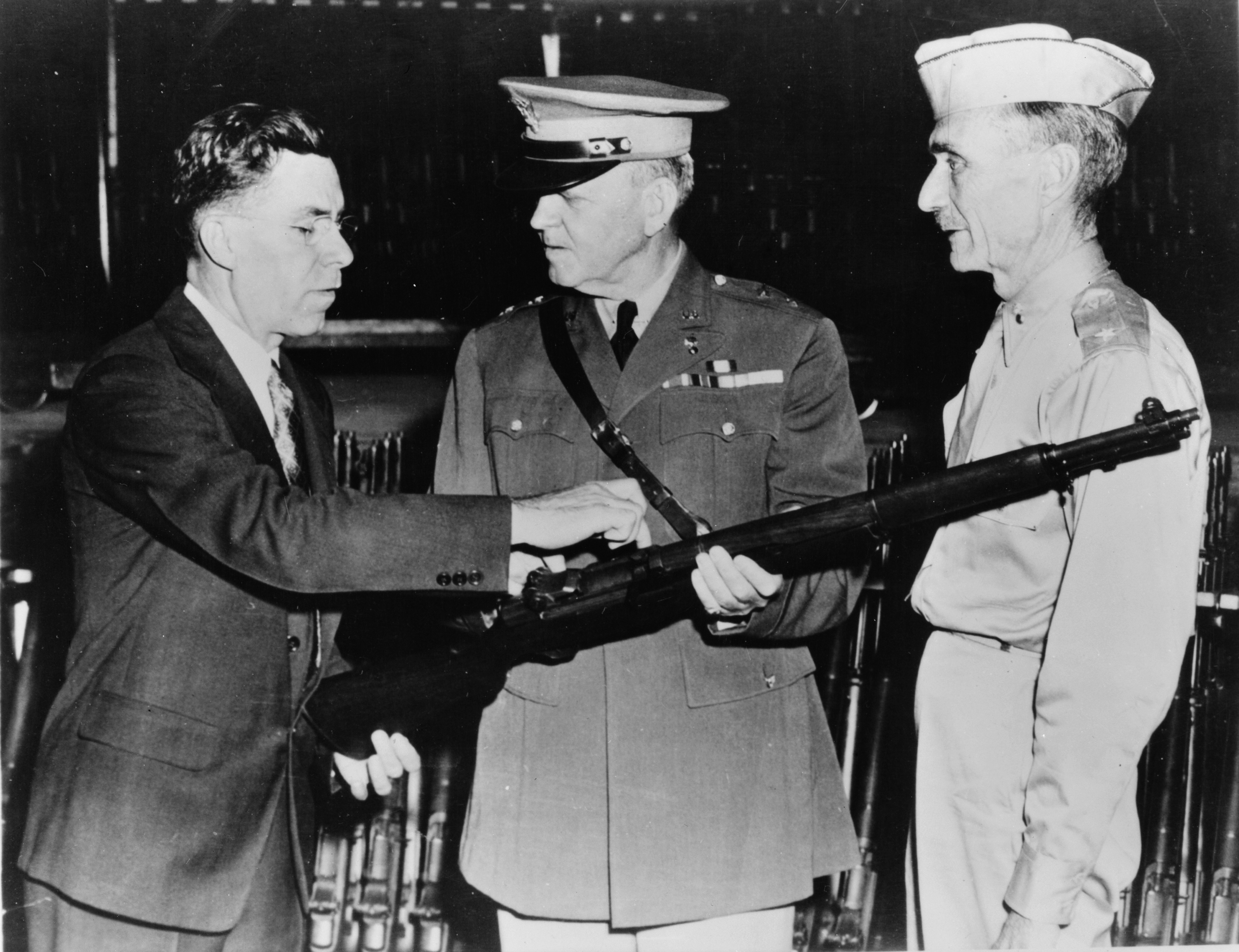 John C. Garand holding a rifle with military officers