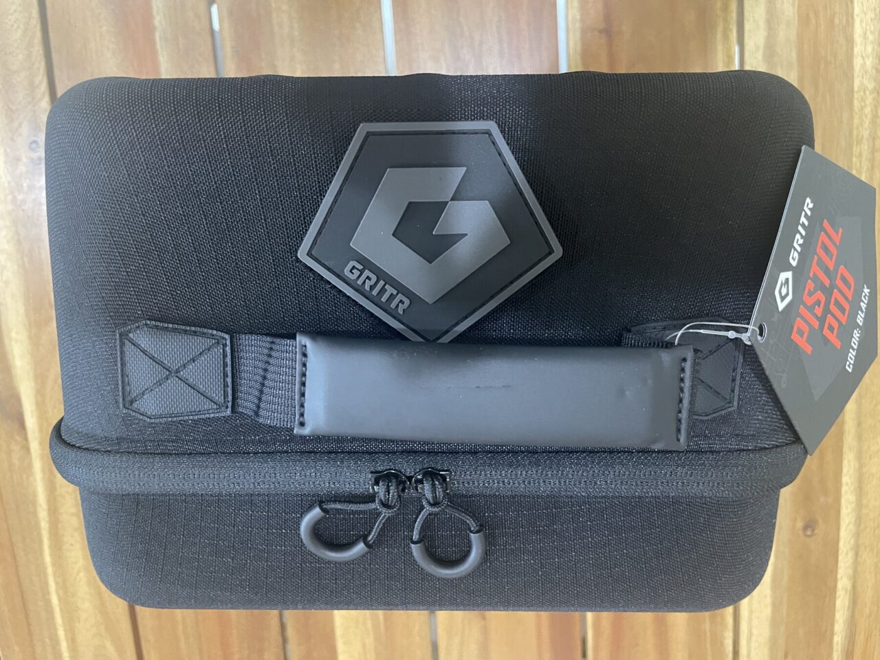 Closed black GRITR Pistol Pod with dual zipper pulls, carrying handle, logo patch, and product tag