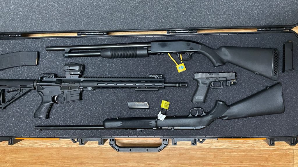 Several guns in a gun case. Two rifles, a pistol, and a shotgun.