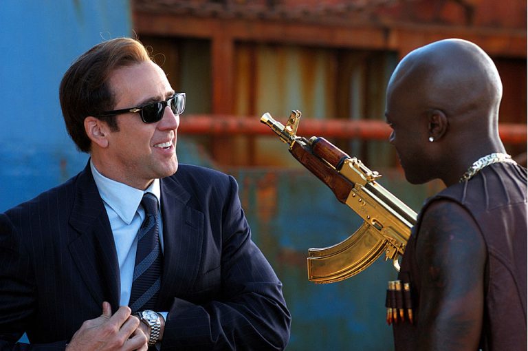 Nicolas Cage as Yuri Orlov in Lord Of War smiling at man with golden AK47