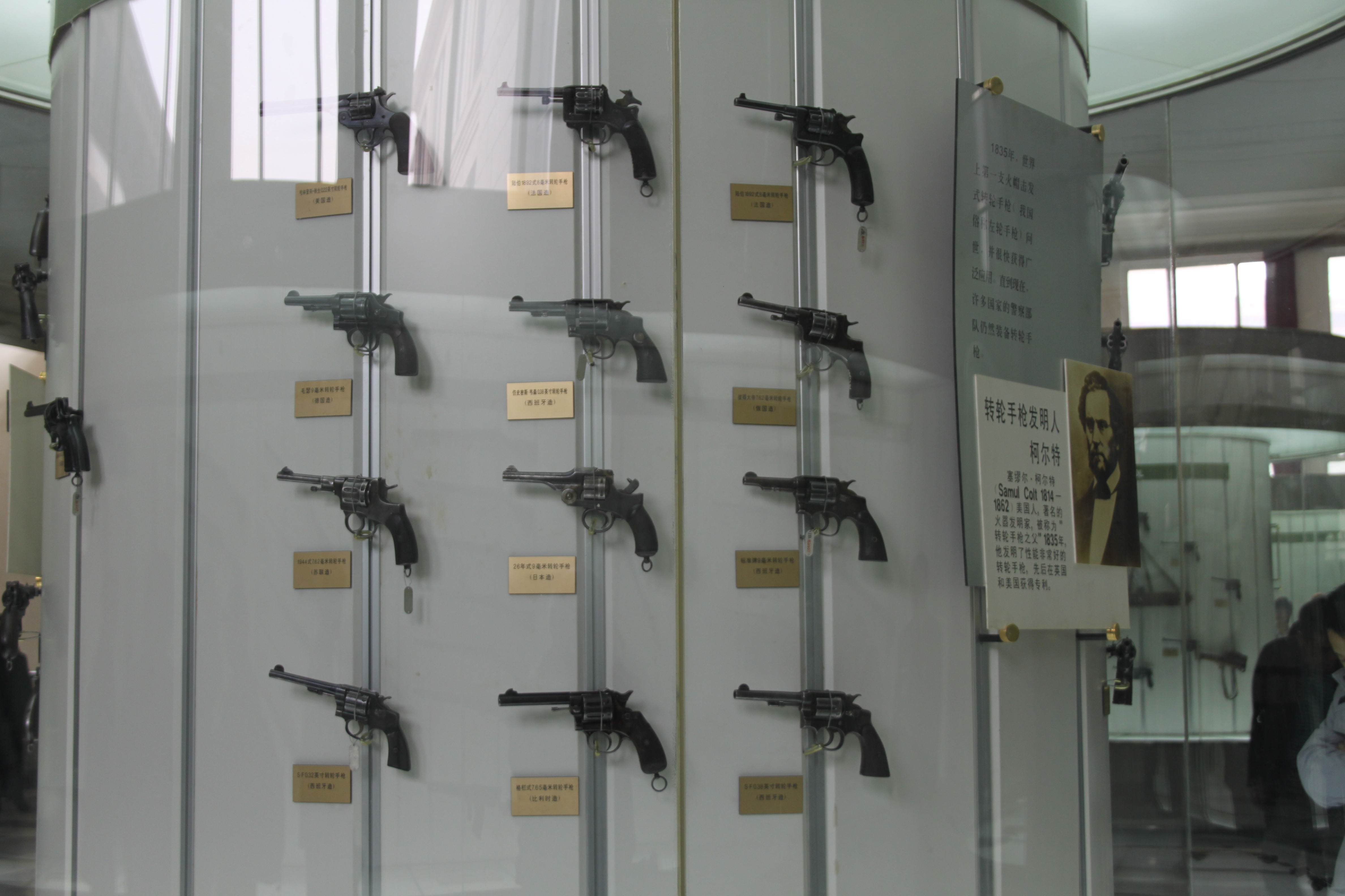 Samuel Colt portrait beside a museum display of Colt pistols