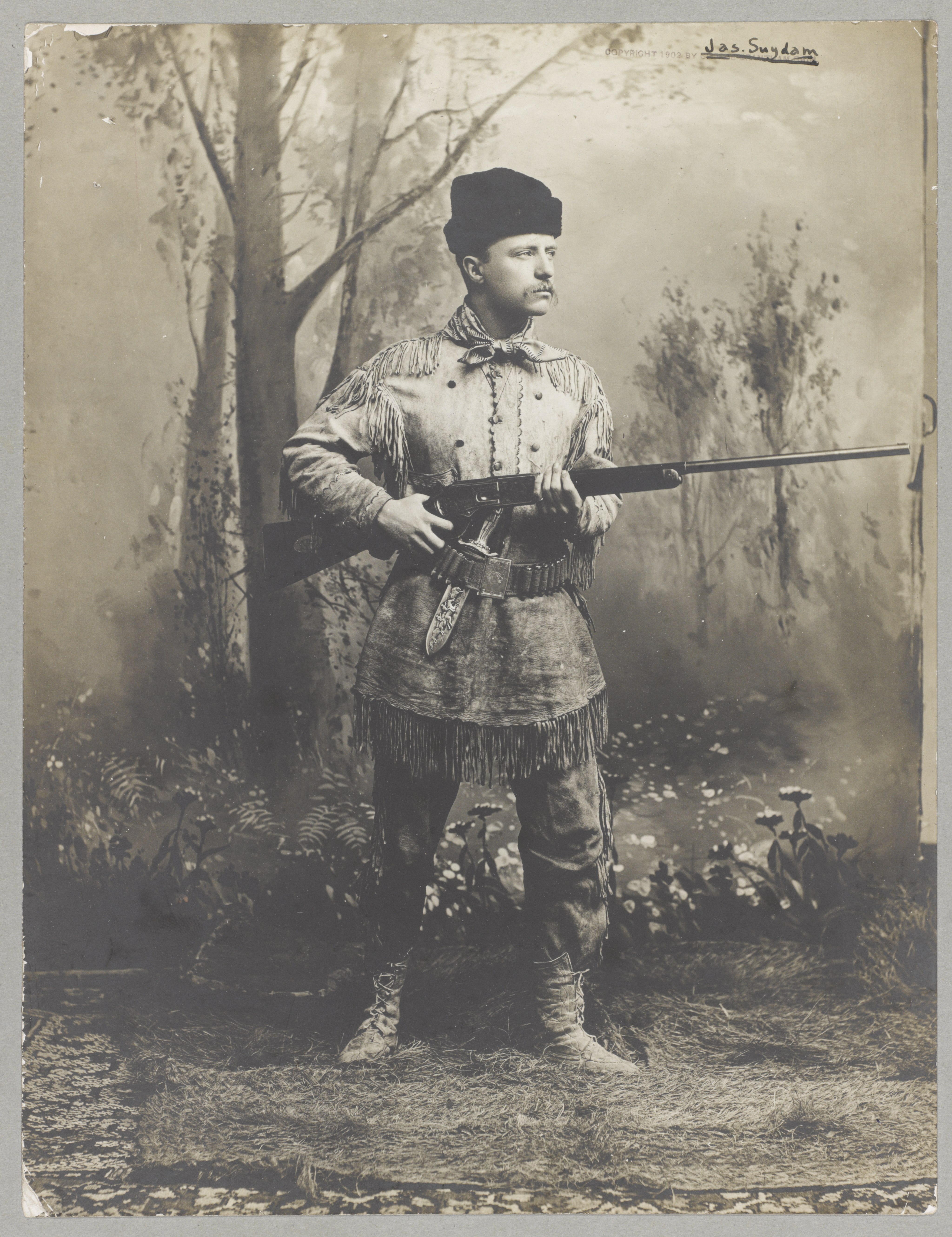 Theodore Roosevelt in a deer-skin hunting suit holding a rifle